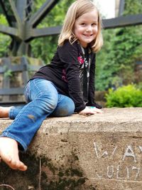 Portrait of smiling girl sitting on retaining wall