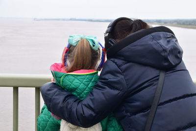 Rear view of siblings standing against sea during winter