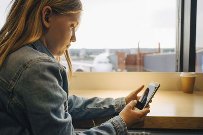 Side view of girl using mobile phone while sitting at airport