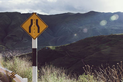 Road sign by mountains against sky