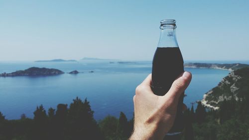 Cropped image of person holding drink against lake