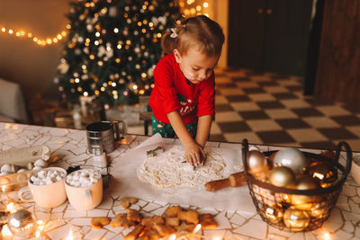 A little girl in red pajamas cooks and eats christmas cookies in the decorated kitchen of the house