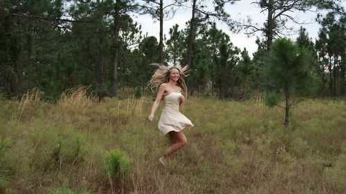 Beautiful blond woman dancing on grassy field against trees at forest