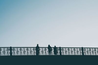 Silhouette people standing on bridge against clear sky