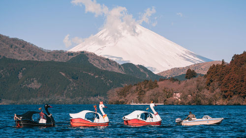 People on boat in lake against mountain range