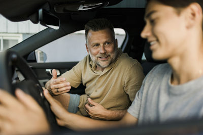 Smiling mature man teaching son to drive while sitting in car