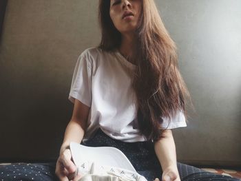 Young woman looking away while sitting against wall at home