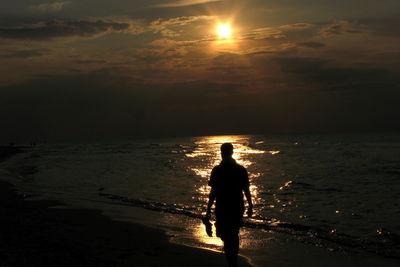 Silhouette man standing on beach against sky during sunset