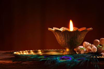 Close-up of oil lamp and peacock feather on wooden table against black background