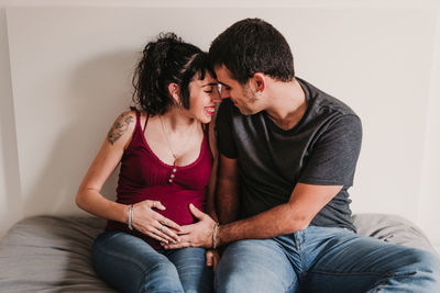 Smiling woman embracing pregnancy with male partner on bed at home