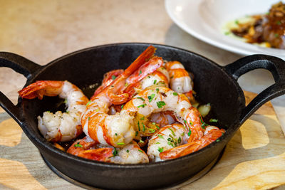 Fried prawns served in black pan on wooden table