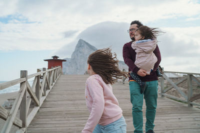 Rear view of father with daughters standing on railing against sky