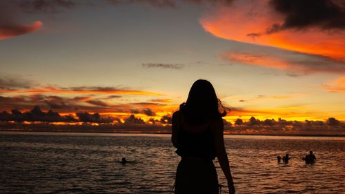 Silhouette woman standing on beach against sky during sunset