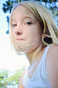 Low angle portrait of girl with short blond hair on sunny day