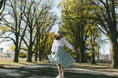 Rear view of young woman spinning on road against trees in park