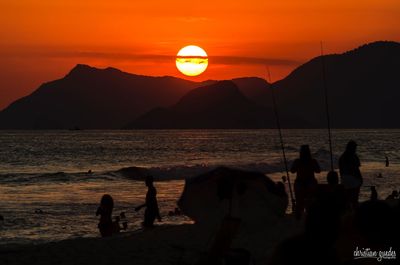 Silhouette people on beach against orange sky