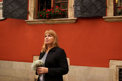 Woman standing on red wall background and holding white flowers. 40s serious woman. copy space.