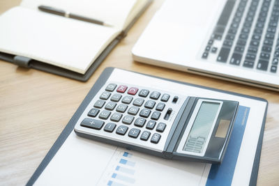 Close-up of calculator on graph by laptop at desk