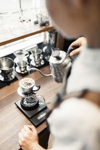 High angle cropped image of barista pouring boiling water in coffee filter at counter