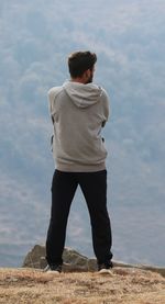 Rear view of man standing on rock against sky