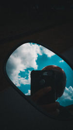 Low angle view of hand holding glass window against sky