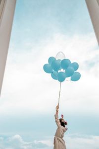 Low angle view of person holding balloons against sky