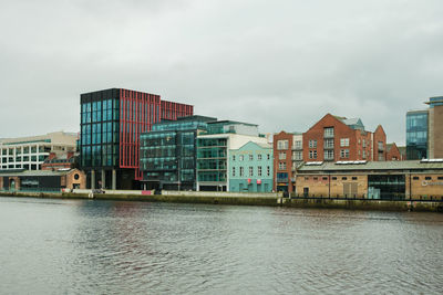 Buildings by river against sky