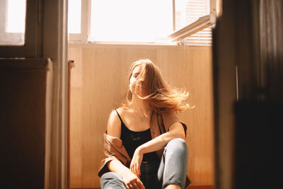 Young woman tossing hair while sitting on floor in balcony at home