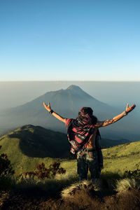 Rear view of person with arms outstretched against mountain range