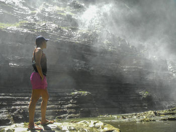 Rear view of young woman standing by rock against sky