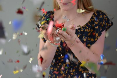 Midsection of woman blowing confetti against gray background