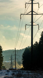 Electricity pylon by trees against sky during sunset