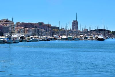 Sailboats moored on sea by buildings against clear blue sky