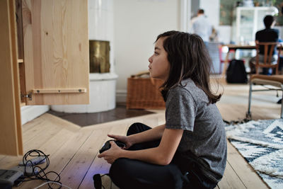 Side view of boy looking away while playing video game on hardwood floor at home