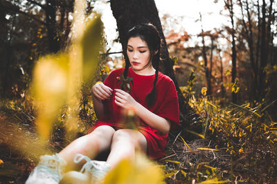 Young woman looking away while sitting on field