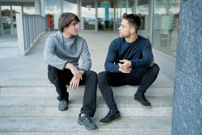 Front view of two young men talking sitting on a city staircase