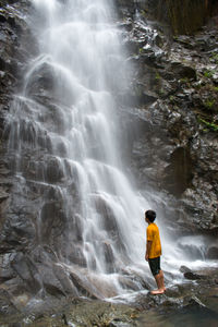 Boy standing in front of waterfall in forest 