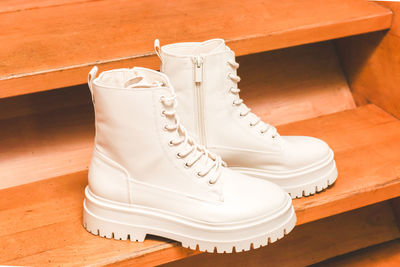 White demi-season boots made of eco-leather with fasteners, laces and rough sole on wooden steps.