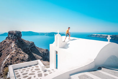 Man standing on whitewashed church roof against clear blue sky