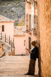 Rear view of woman standing on mobile phone against building