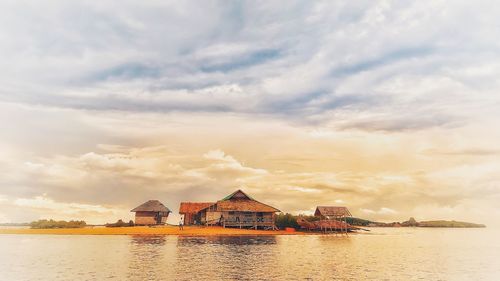 Houses by sea against sky during sunset