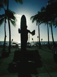Silhouette man photographing palm tree by sea against sky