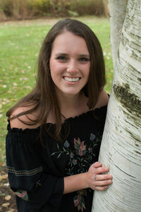 Portrait of smiling young woman standing by tree trunk