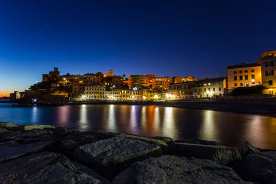 River by illuminated buildings against sky at dusk