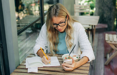Business woman working during lunch using zoom on phone and notepad.
