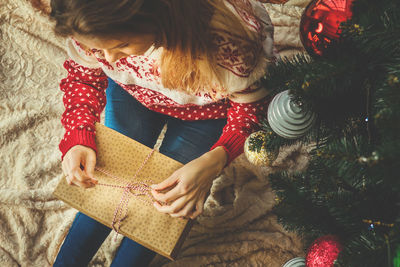 High angle view of woman opening gift by christmas tree