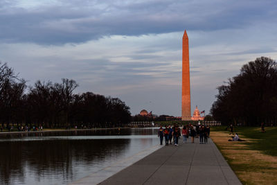 People walking in park against cloudy sky