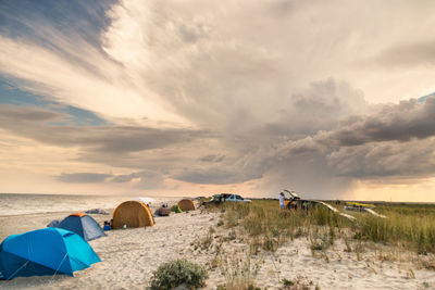 Tents at sandy beach against cloudy sky during sunset