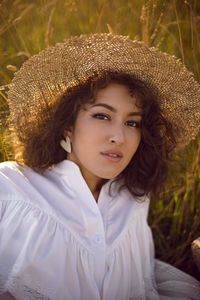 Portrait of a woman in white clothes and in a wicker hat lying on a field with grass in autumn.