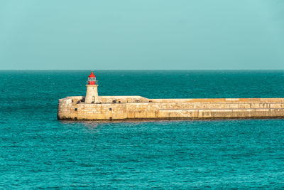 Lighthouse on sea by building against sky